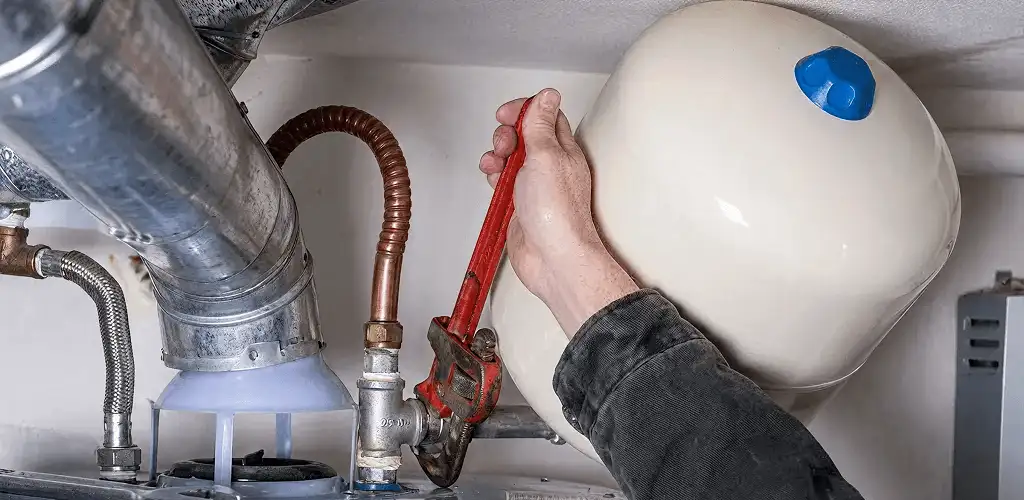 Water heater repair technician tightening plumbing connections near a tank unit in Green Bay, WI